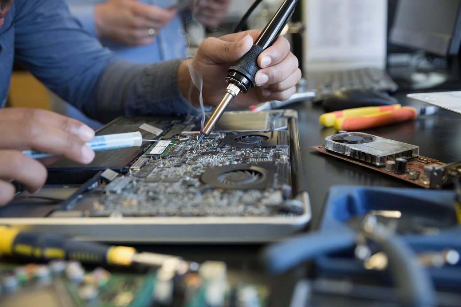 Technician soldering a component onto a laptop motherboard at the GadgyFix bench